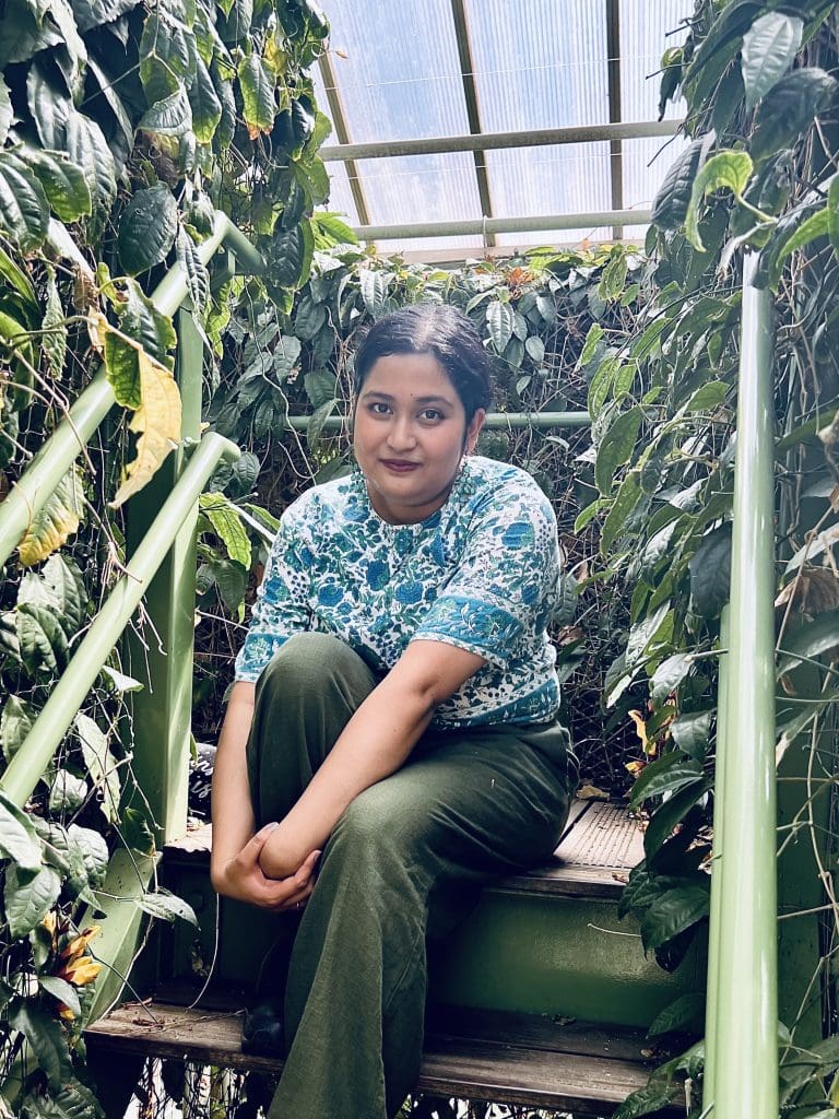 woman with hair pulled back sitting on steps surrounded by greenery