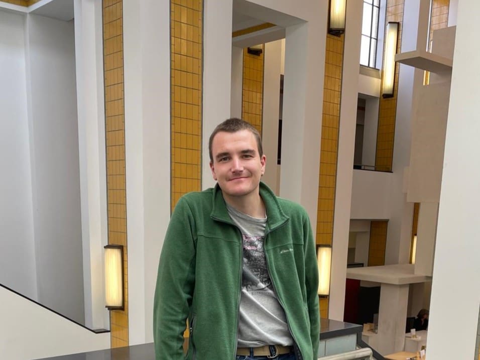 man standing inside a building smiling wearing a green jacket