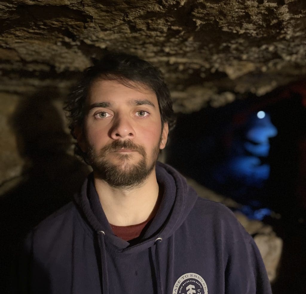 A man with dark hair and facial hair looking straight at the camera