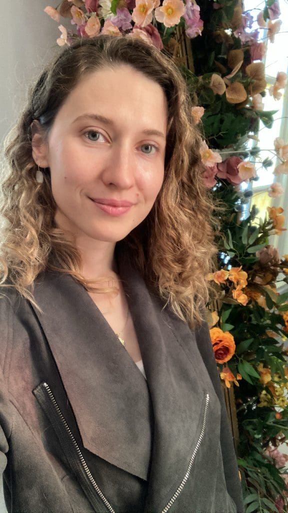 a woman smiling standing in front of a flower arch 